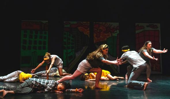 A group of students dance on a stage inside a theatre. 